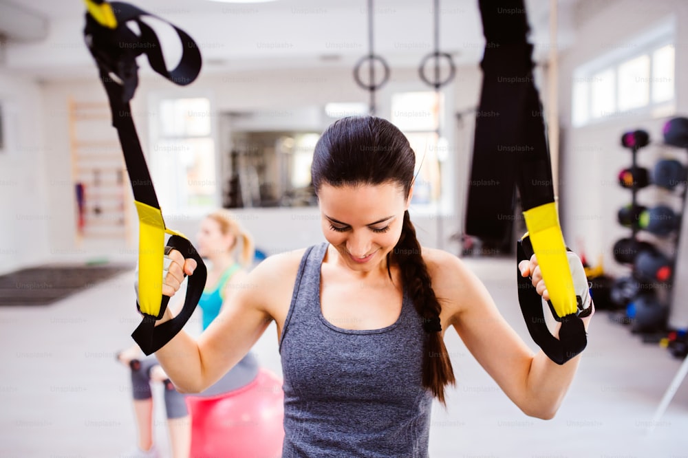 Ajuste a mulher atraente nos braços de treinamento da academia com tiras de fitness trx