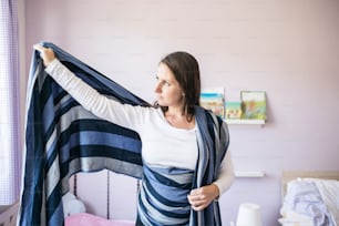 Belle jeune mère enroulant une écharpe de portage pour bébé autour d’elle dans sa chambre