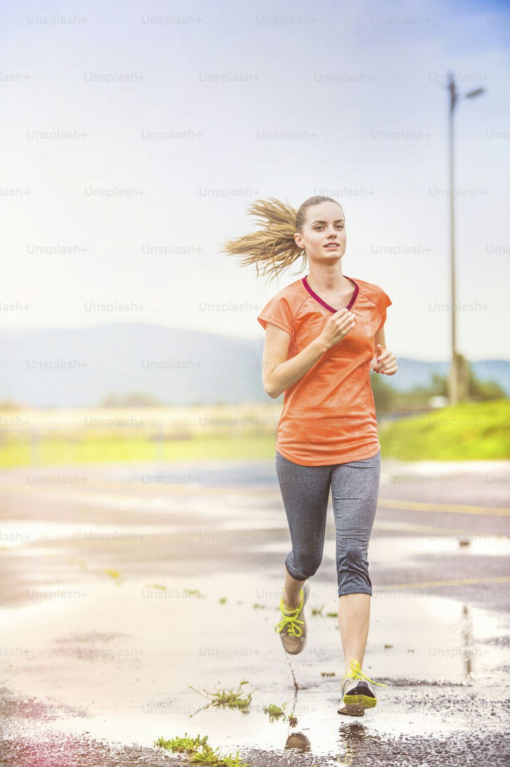 Young woman jogging on asphalt in rainy weather