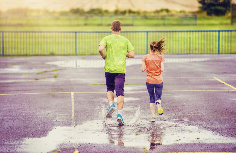 Young couple jogging on asphalt in rainy weather