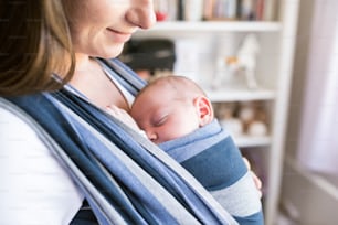 Close up of unrecognizable young mother with her newborn baby son in sling at home