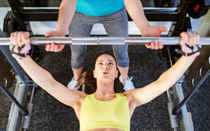 Woman with her personal trainer in a gym working out with weights, bench pressing