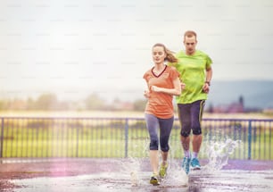 Junges Paar joggt bei Regenwetter auf Asphalt