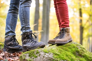 Primer plano de las piernas de un hombre y una mujer irreconocibles en la naturaleza otoñal de pie sobre una roca cubierta de musgo verde. Zapatos para caminar.