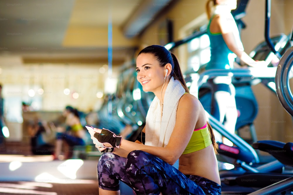 Attractive fit women in a gym with smart phone against a row of treadmills