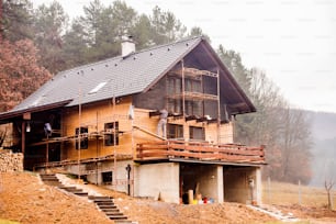 Bauarbeiter steht auf Gerüst, wärmedämmendes Haus mit Glaswolle und schwarzer Folie, Holzfassade.