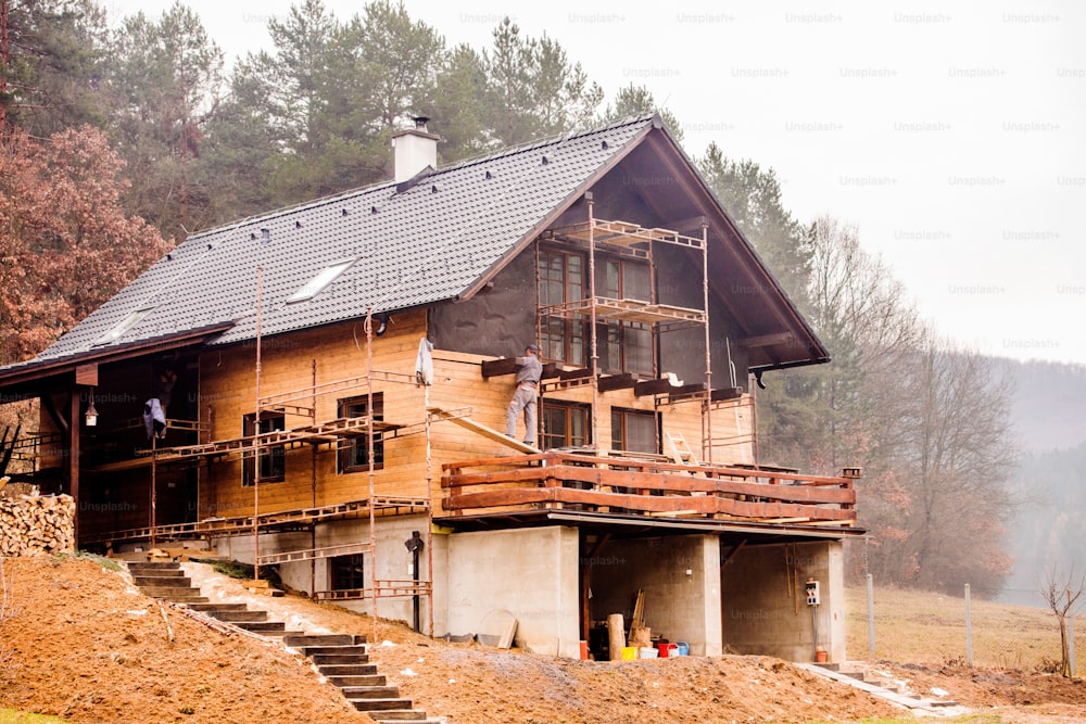 足場の上に立つ建設作業員、グラスウールと黒箔で断熱された家、木製のファサードを行う。