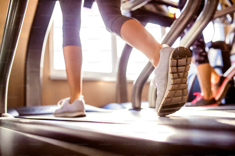 Close up of legs of woman running on treadmills gym, sunny day