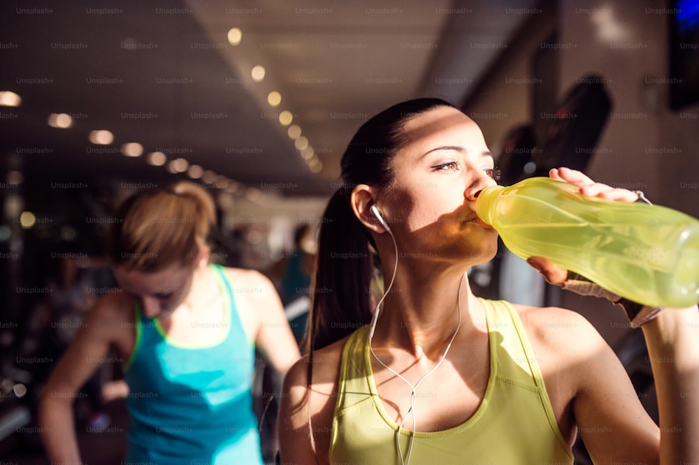Attractive fit woman in gym drinking water from bottle, sunny day
