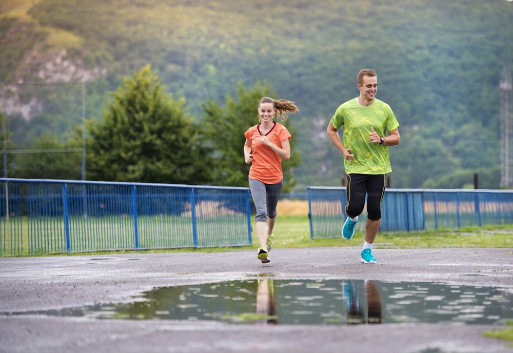 Young couple jogging on asphalt in rainy weather