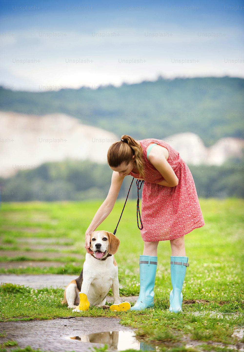 Jeune femme en robe et bottes en caoutchouc turquoise promener son chien beagle dans un parc