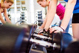 Close up of two attractive fit women in gym working out with weights
