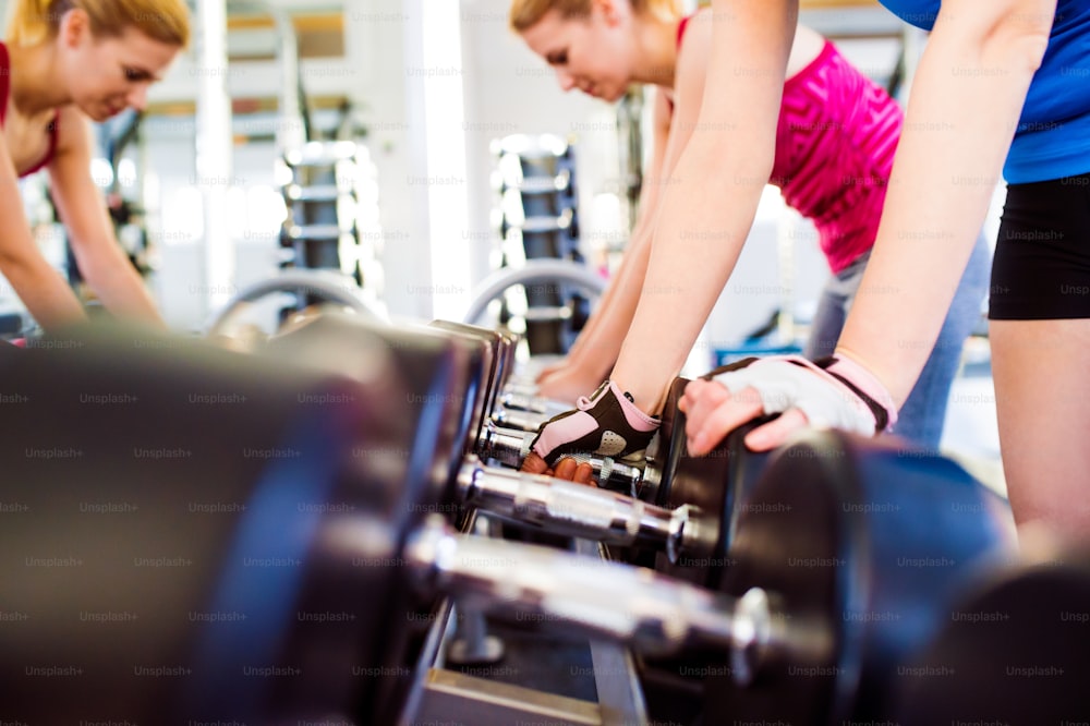 Nahaufnahme von zwei attraktiven, fitten Frauen im Fitnessstudio, die mit Gewichten trainieren