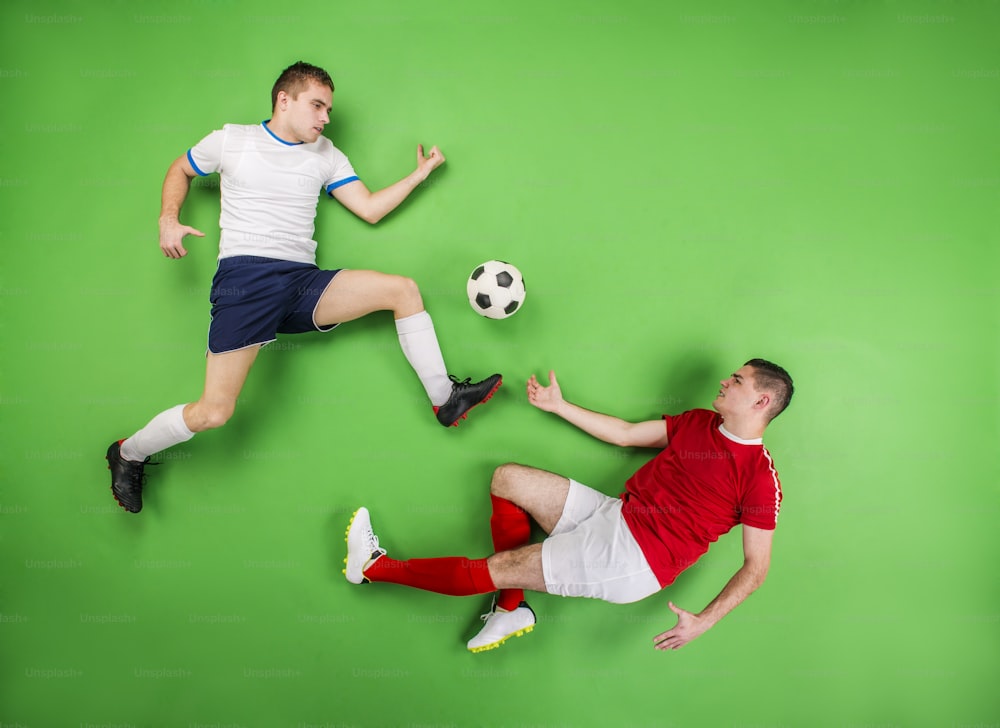 Two football players fighting for a ball. Studio shot on a green backgroud.