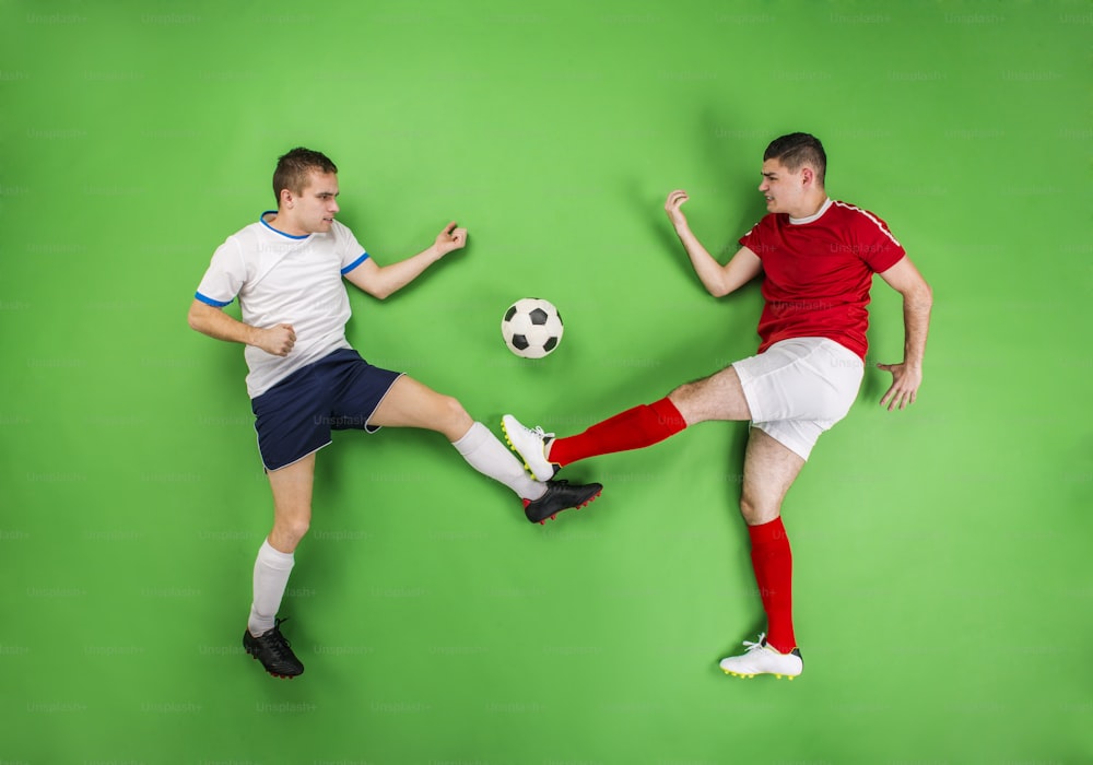 ボールを奪い合う2人のサッカー選手。緑の背景でスタジオ撮影。