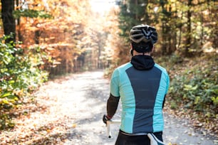 Junger gutaussehender Sportler fährt draußen Fahrrad in sonniger Herbstnatur, Kopfhörer in den Ohren, Rückansicht