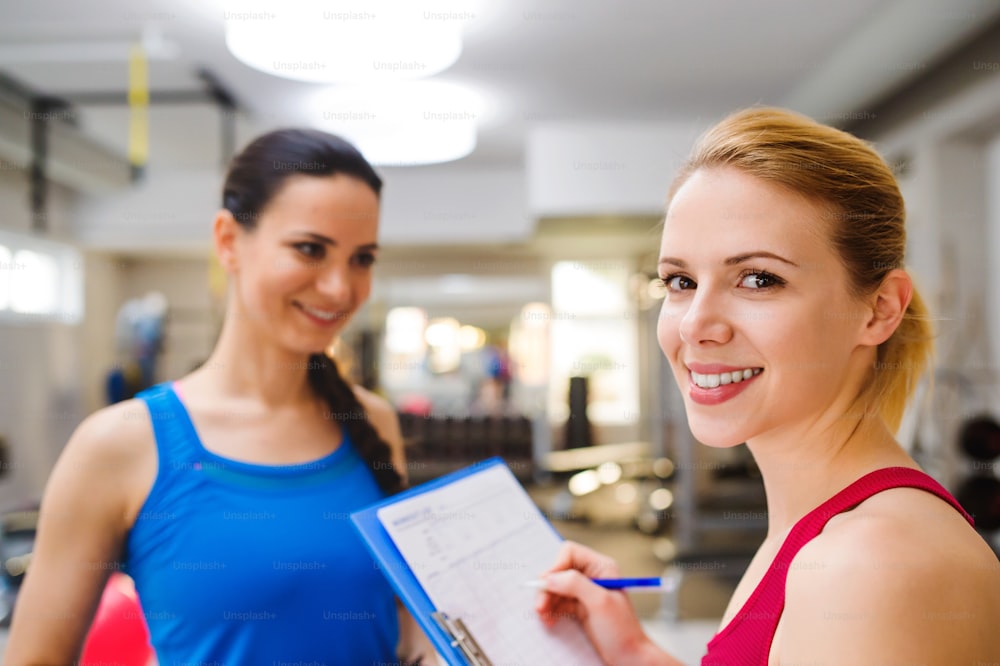 Primo piano, attraente donna in forma in una palestra consulenza lavorare fuori con personal trainer, piano di esercizi sugli appunti