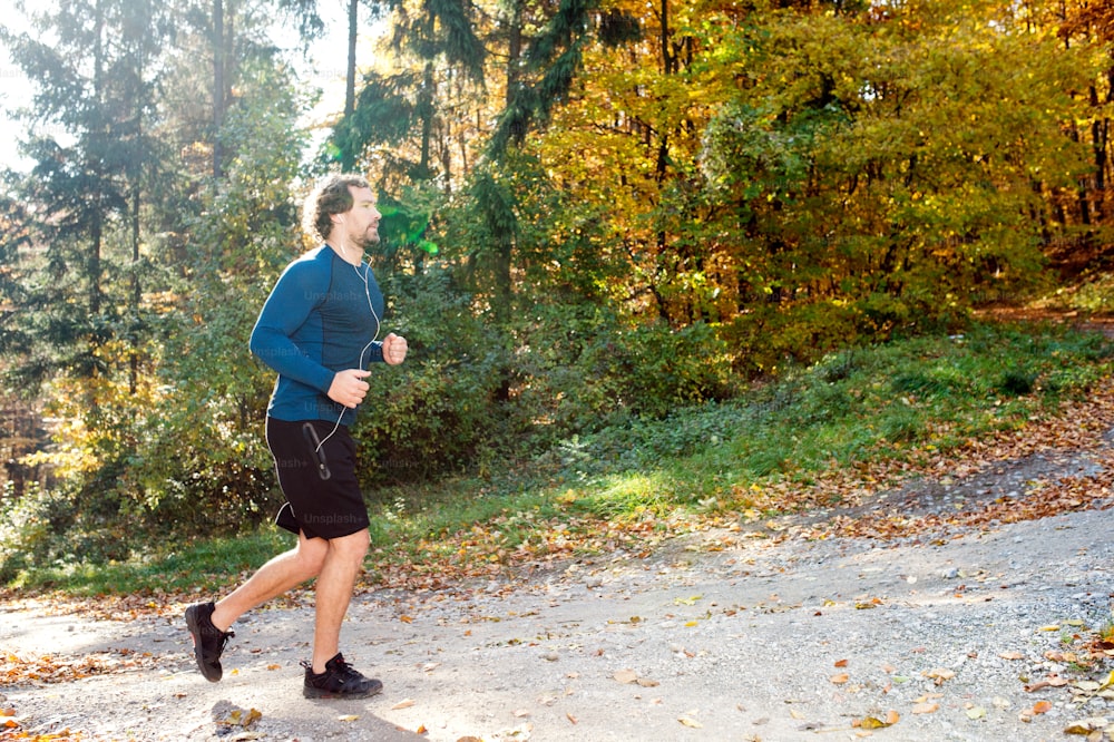Young handsome runner with earphones in his ears, listening music, outside in sunny autumn nature
