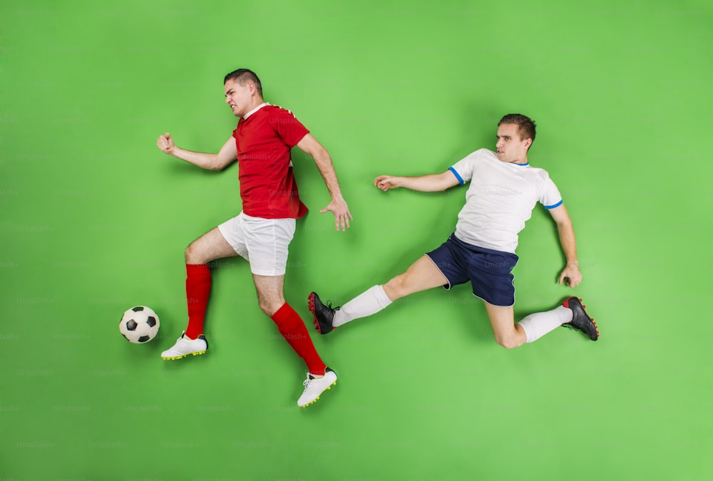 Two football players fighting for a ball. Studio shot on a green backgroud.