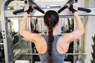 Close up of attractive fit woman flexing back muscles on cable machine, back view, rear viewpoint