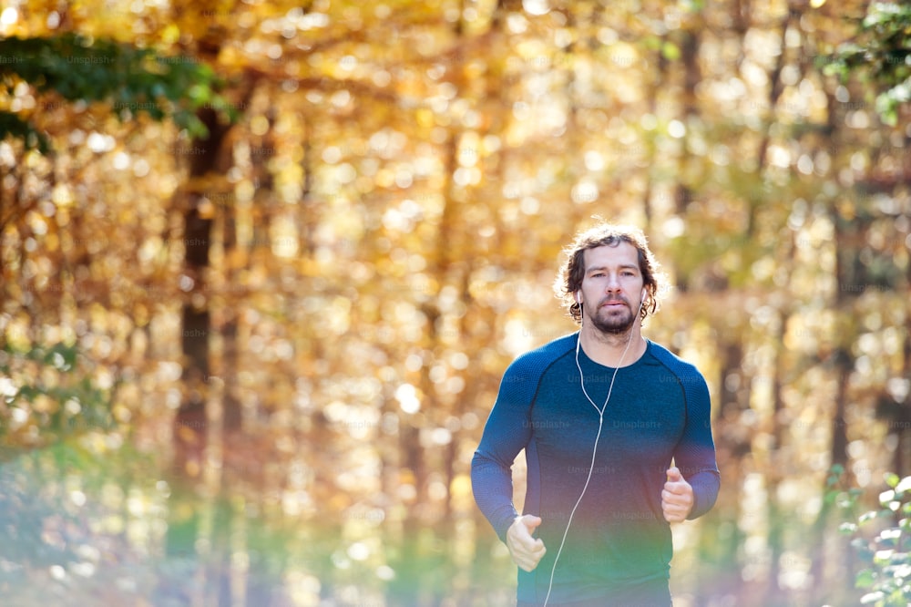 Young handsome runner with earphones in his ears, listening music, outside in sunny autumn nature