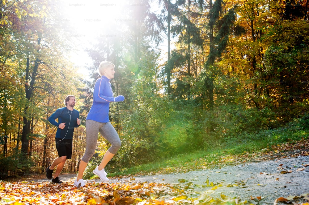 Beautiful couple running together outside in sunny autumn forest