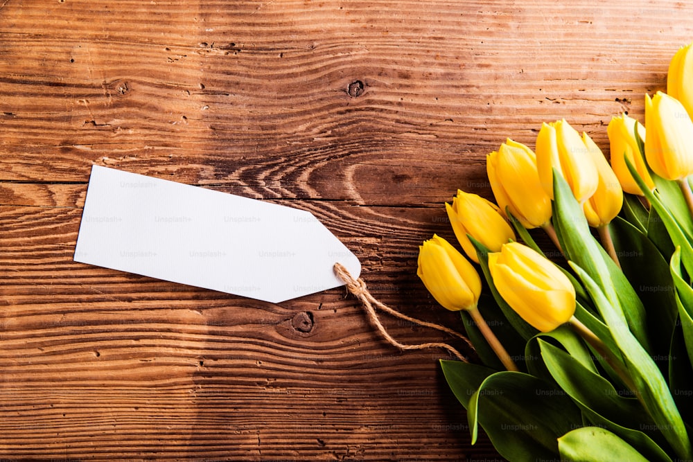 Bouquet of yellow tulips with empty paper tag. Studio shot on wooden background.