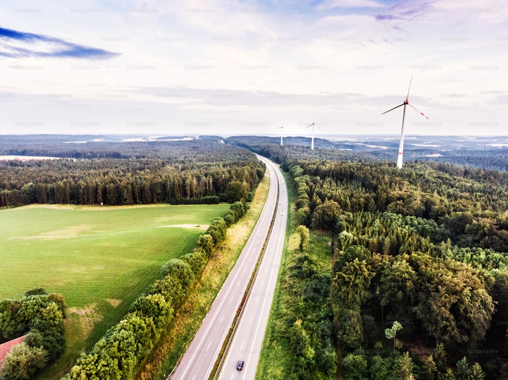 Aerial view of highway and windmills in the middle of green forest. Cloudy sky. Netherlands