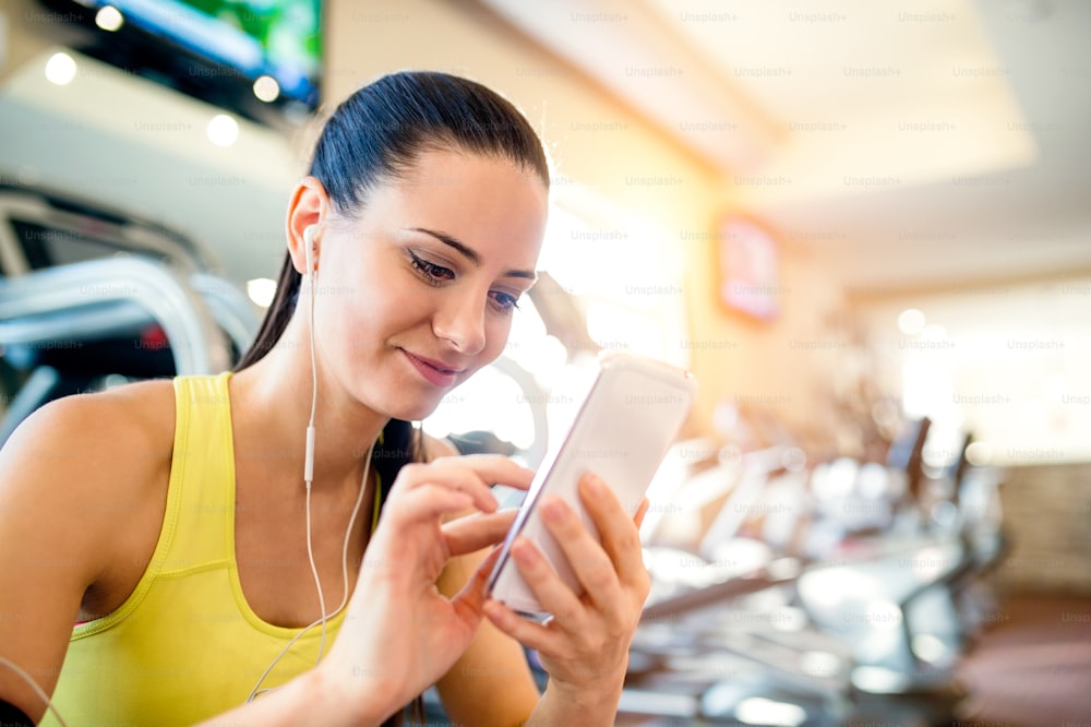 Mulher atraente em um ginásio com telefone inteligente contra uma fileira de esteiras