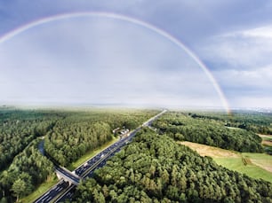 Aerial view of highway full of cars and trucks in the middle of green forest, colorful rainbow, city. Netherlands