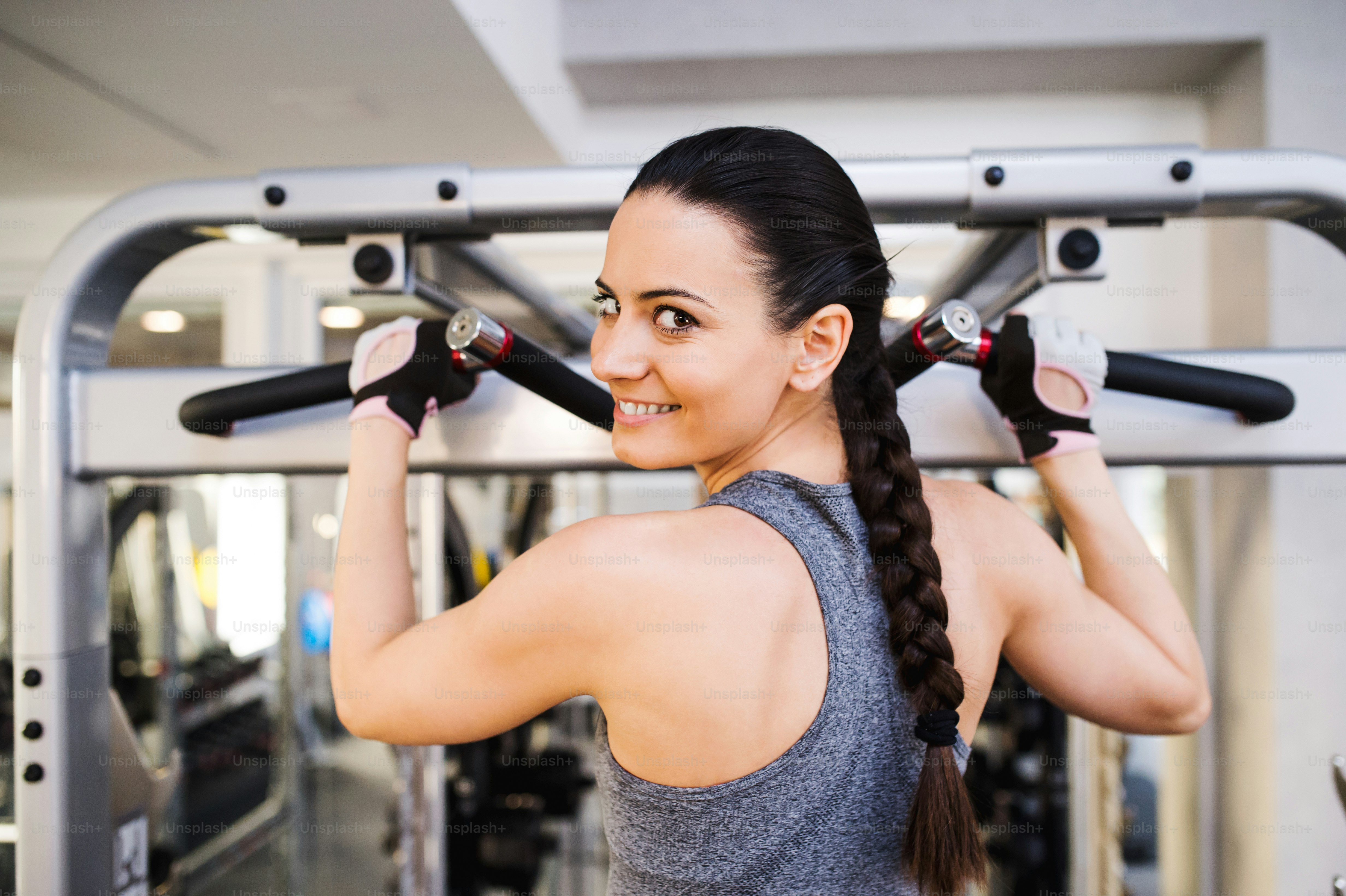 Close up of attractive fit woman flexing back muscles on cable machine, back view, rear viewpoint