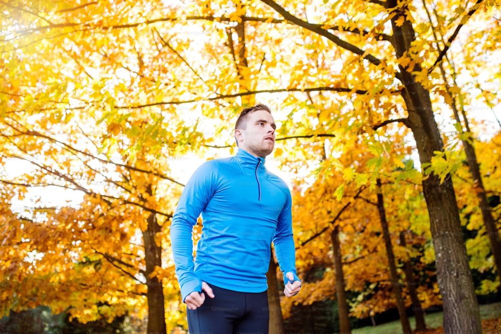Young handsome hipster athlete in blue sweatshirt running outside in colorful sunny autumn nature