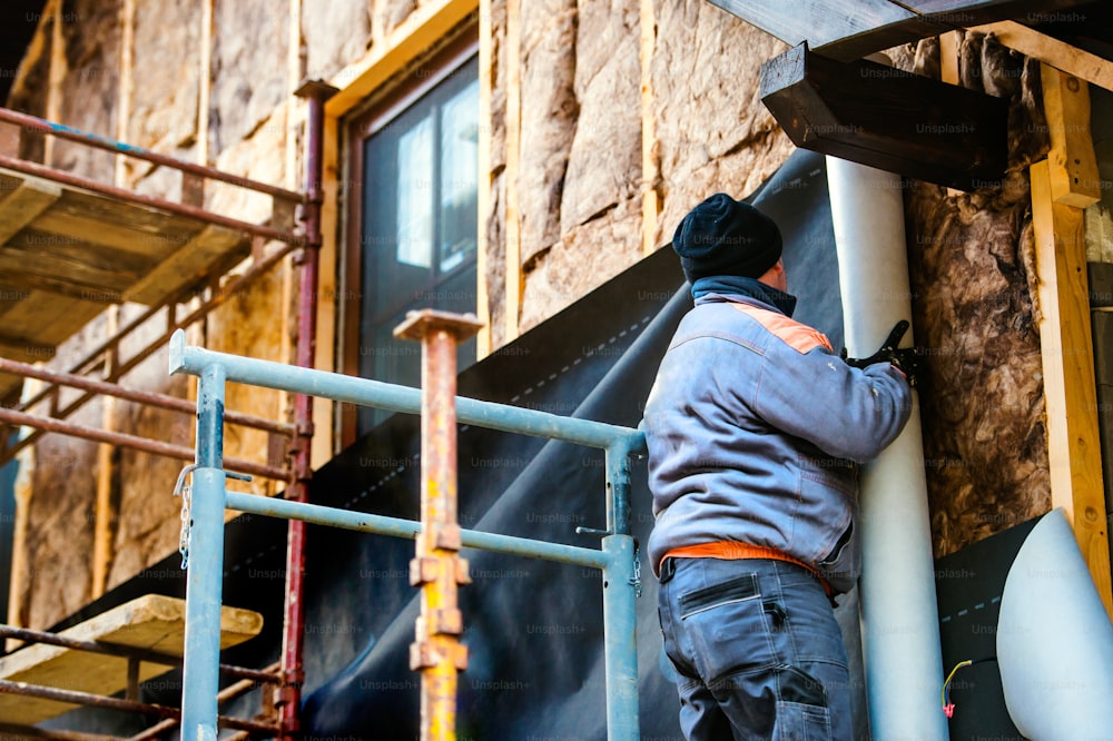 Bauarbeiter auf Gerüst wärmedämmende Hausfassade mit Glaswolle und schwarzer Folie.