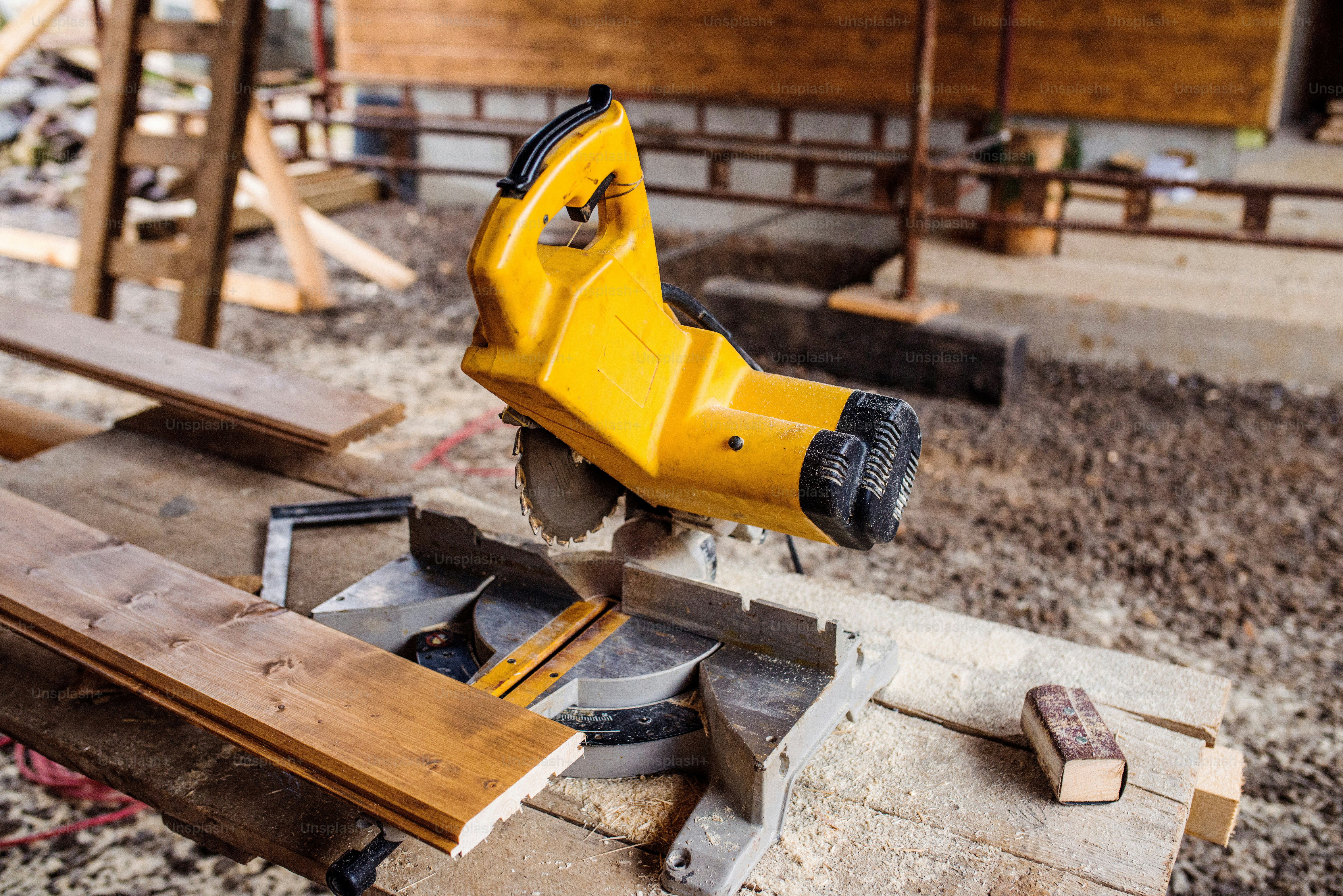 Close up of yellow circular saw laid on table, stack of wood behind it