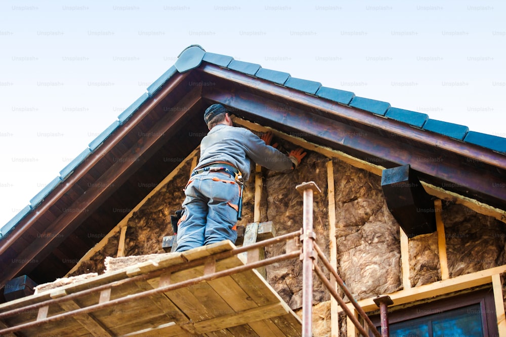 유리솜으로 단열 집 외관을 단열하는 비계 위에 서 있는 건설 노동자.