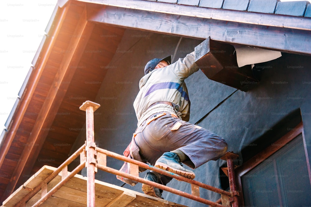 Ouvrier du bâtiment debout sur un échafaudage isolant thermiquement la façade de la maison avec de la laine de verre et une feuille noire.