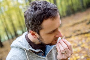 Young hipster man picking mushrooms in autumn forest, smelling it, identifying it