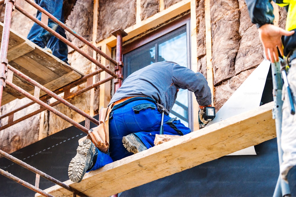Close up de trabalhadores da construção em pé em andaime termicamente isolando a fachada da casa com lã de vidro.