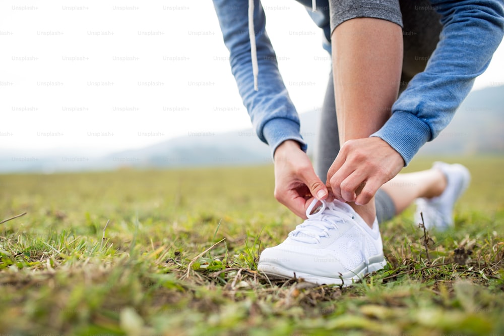 Close up of an unrecognizable young runner tying shoelaces, autumn nature