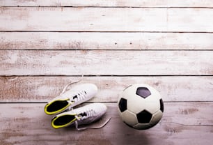 Soccer ball, cleats against wooden floor, studio shot on white background. Flat lay, copy space