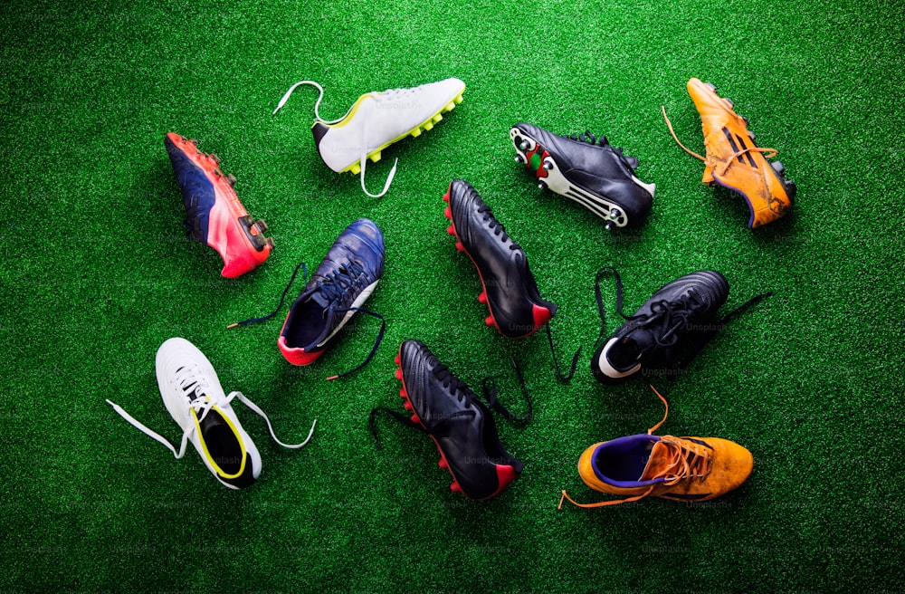 Various colorful cleats against artificial turf, studio shot on green background. Flat lay.