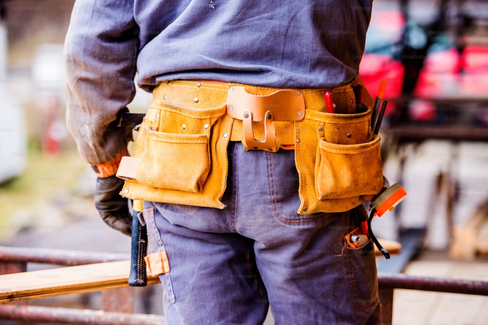 Primer plano de un trabajador de la construcción irreconocible con una bolsa de herramientas en el sitio, vista trasera