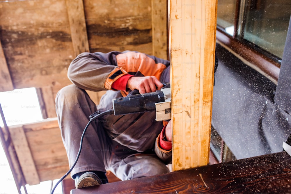 Carpinteiro com moedor. Homem moendo tábuas de madeira para construção de casas.