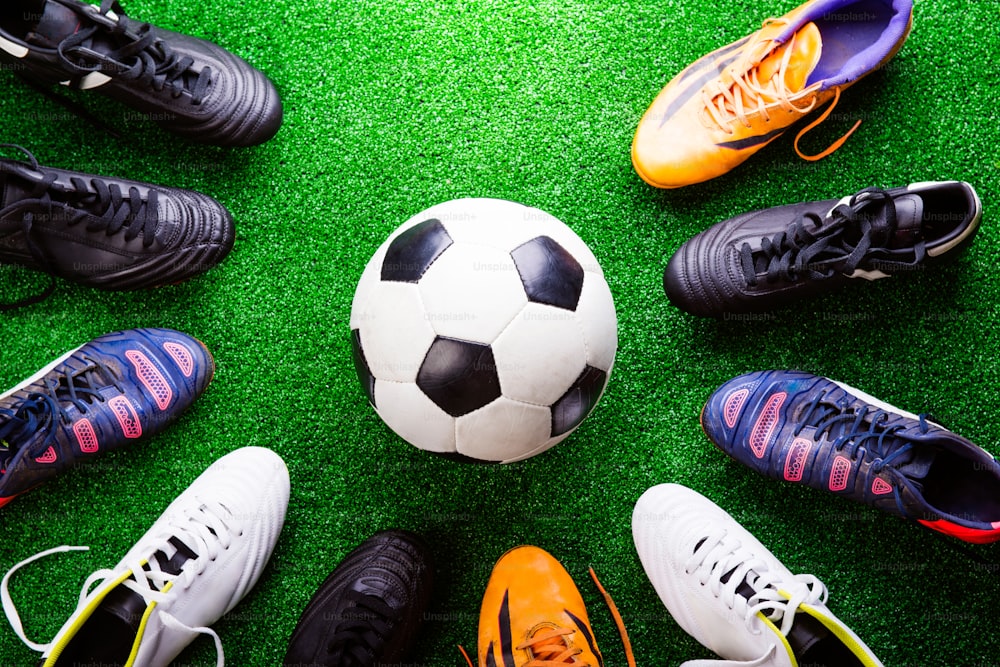 Soccer ball and cleats against artificial turf, studio shot on green background.