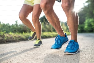 Unrecognizable senior couple running outside in green sunny summer nature. Close up.