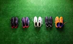 Various colorful cleats against artificial turf, studio shot on green background. Flat lay, copy space.