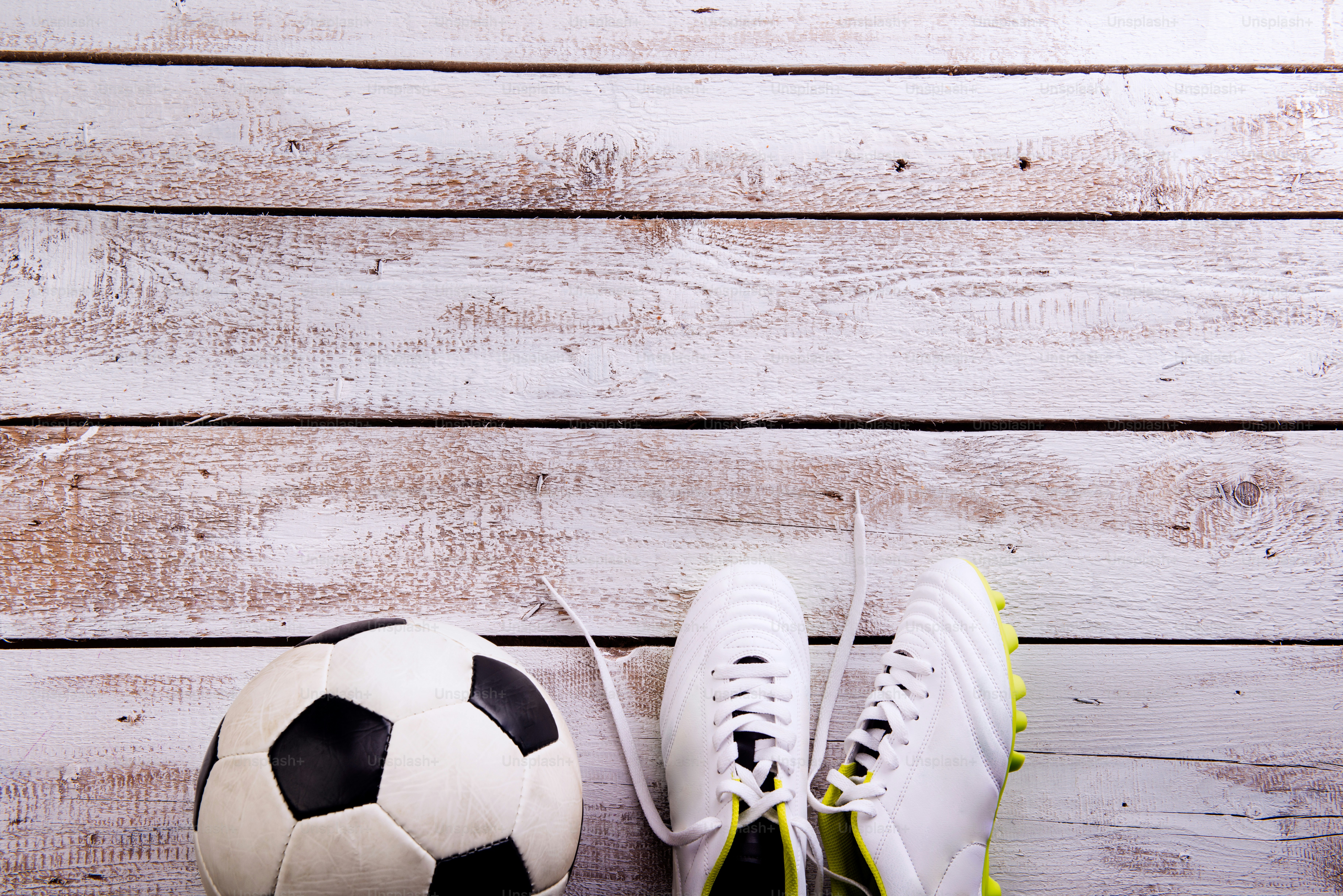 Soccer ball, cleats against wooden floor, studio shot on white background. Flat lay, copy space
