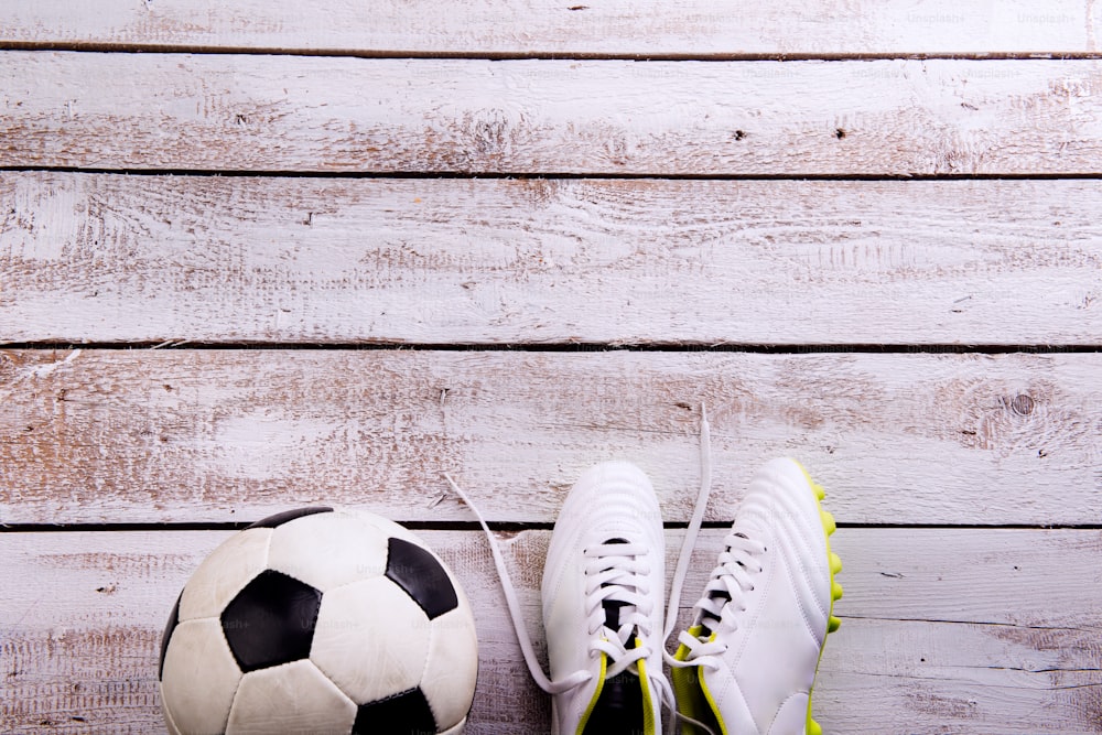 Fußball, Stollenschuhe gegen Holzboden, Studioaufnahme auf weißem Hintergrund. Flaches Lay, Kopierraum
