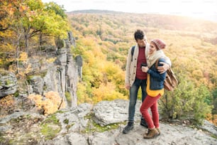 Beau jeune couple sur une promenade, debout sur un rocher contre la forêt d’automne colorée, femme tenant des jumelles