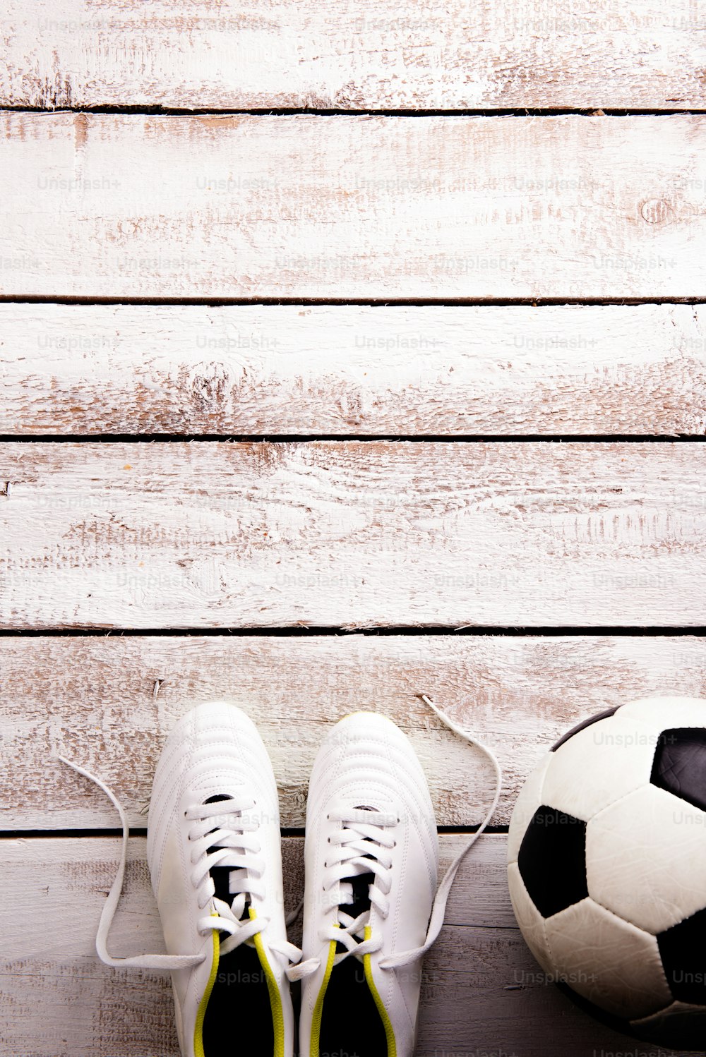 Pallone da calcio, tacchetti contro pavimento in legno, girato in studio su sfondo bianco. Flat lay, spazio di copia